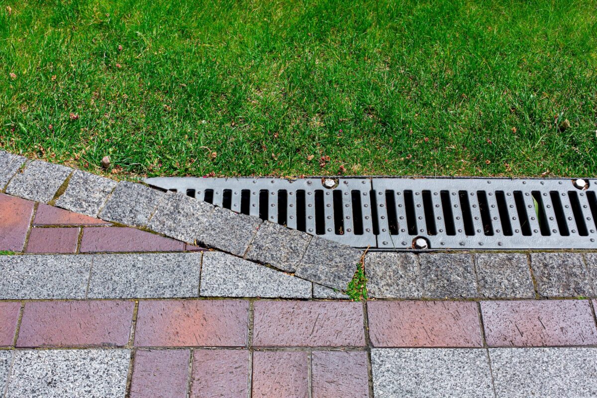 Drainage grate bolted to storm drain at corner of pavement walkway
